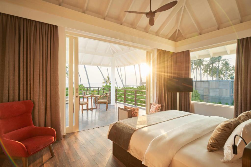 a bedroom with a bed and a chair and a balcony at Siyam World Maldives - 24-Hour Premium All-inclusive with Free Transfer in Dhigurah