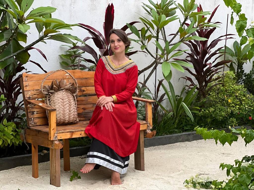 Una mujer con un vestido rojo sentada en un banco en Veli Thoddoo Inn, en Thoddoo