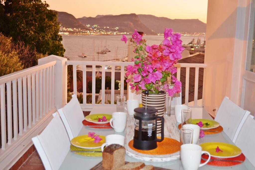 una mesa con platos de comida y flores en el balcón en Bougainvillea House - The Heart of Simonstown, en Simonʼs Town