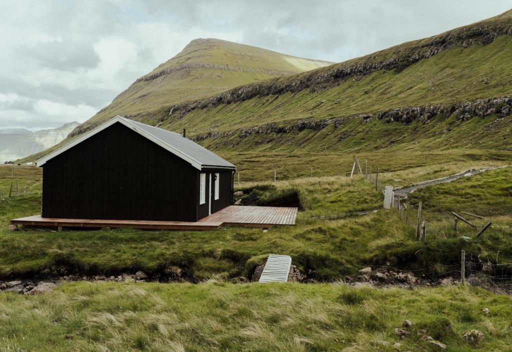 a black house in a field with a hill at Authentic Cabin - Unique location - In nature - 2BR in Hellur