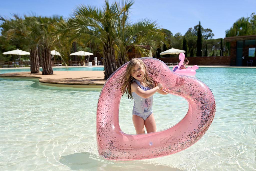 a little girl is standing inside of a pink raft in the water at Camping Campo dei Fiori in Vada