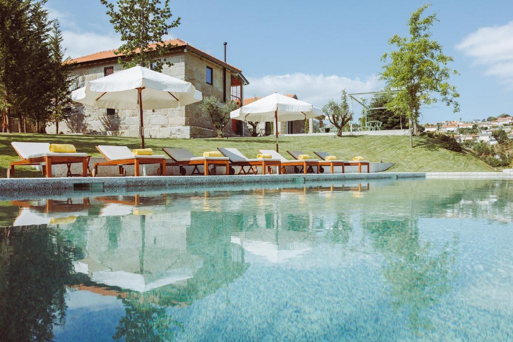 a swimming pool with chairs and umbrellas next to a house at Oliveiras Village — Agroturismo in Amarante