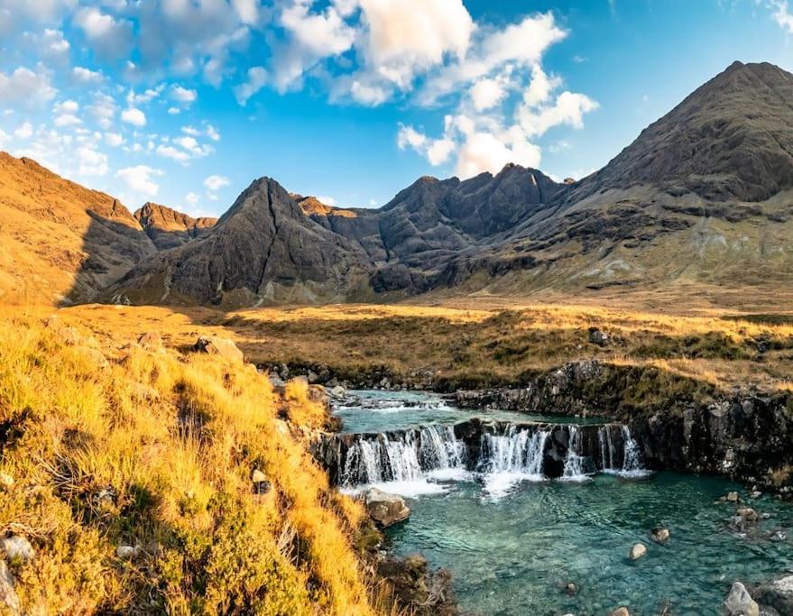 a waterfall in a field with mountains in the background at This must be the place - Skye, Carbost in Carbost