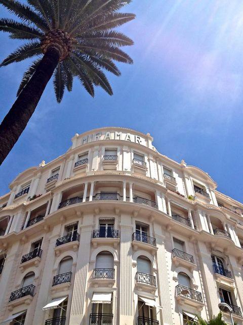 un grand bâtiment avec un palmier devant lui dans l'établissement Studio de luxe Miramar, à Cannes