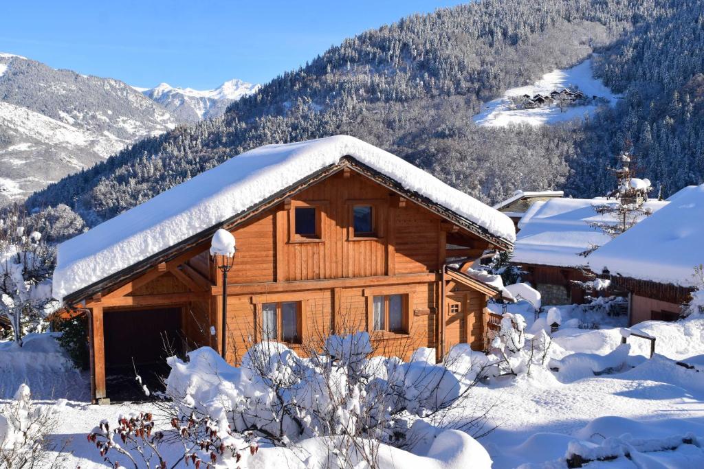 una cabaña de madera cubierta de nieve con montañas al fondo en Chalet et studio "La Fée des Neiges" en Méribel