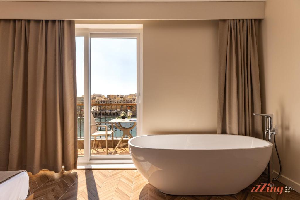 a large white bath tub in a room with a balcony at El Doris Boutique Living in Marsaskala