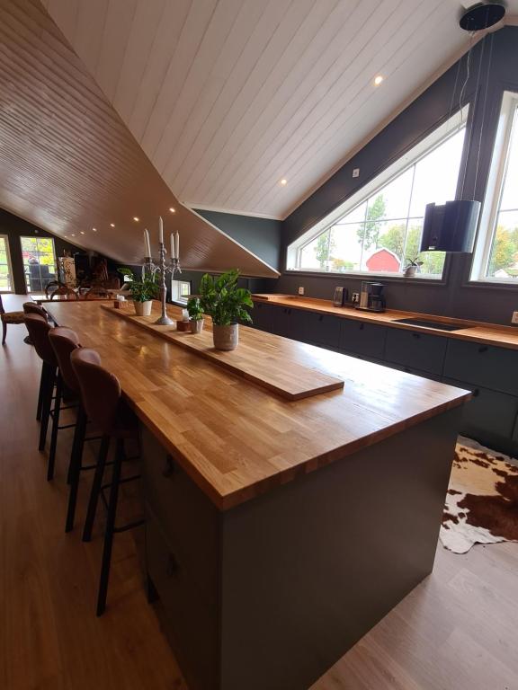 uma grande cozinha com um longo bar de madeira com bancos em Mysig lägenhet med öppen planlösning på hästgård. em Ljung