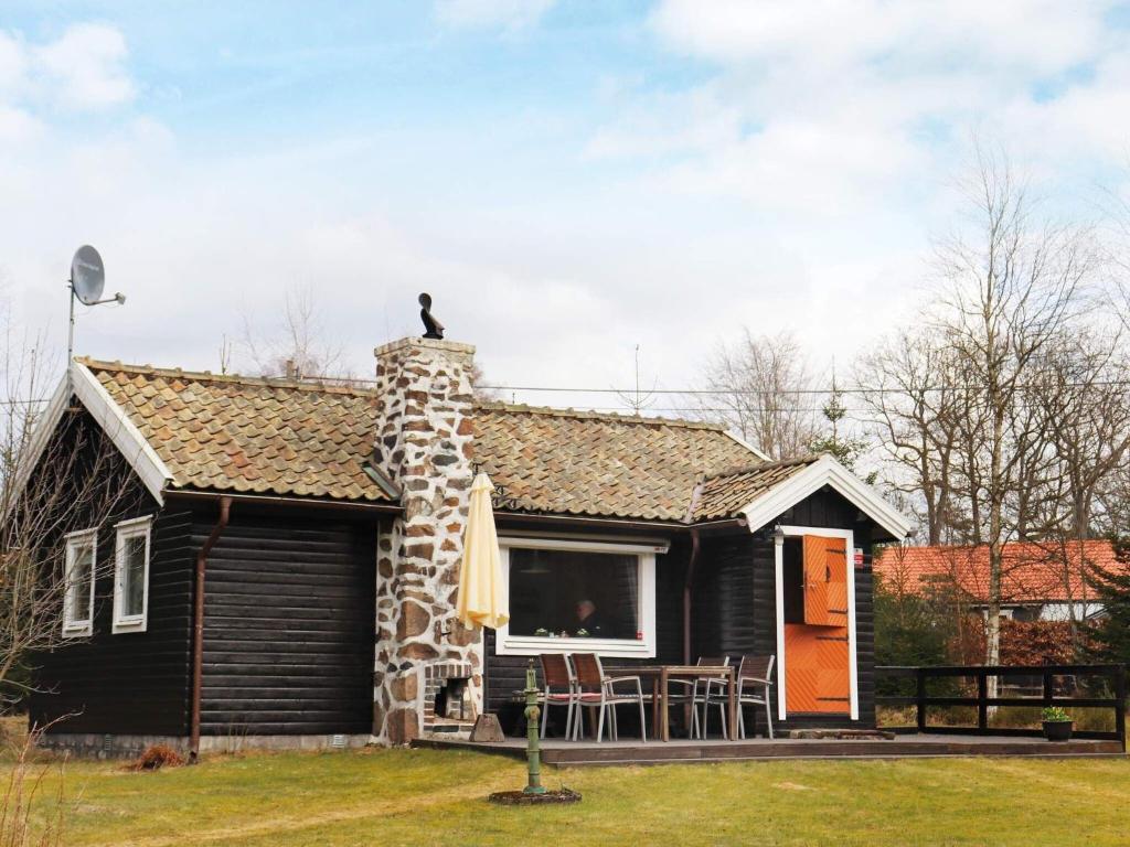 a small black house with a stone chimney at Holiday home MUNKA-LJUNGBY III in Munka-Ljungby