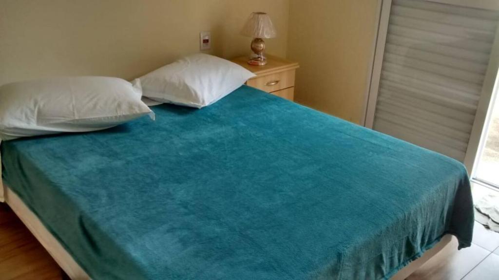 a bed with a blue blanket and two pillows at Suíte residencial com entrada independente em Itatiba in Itatiba
