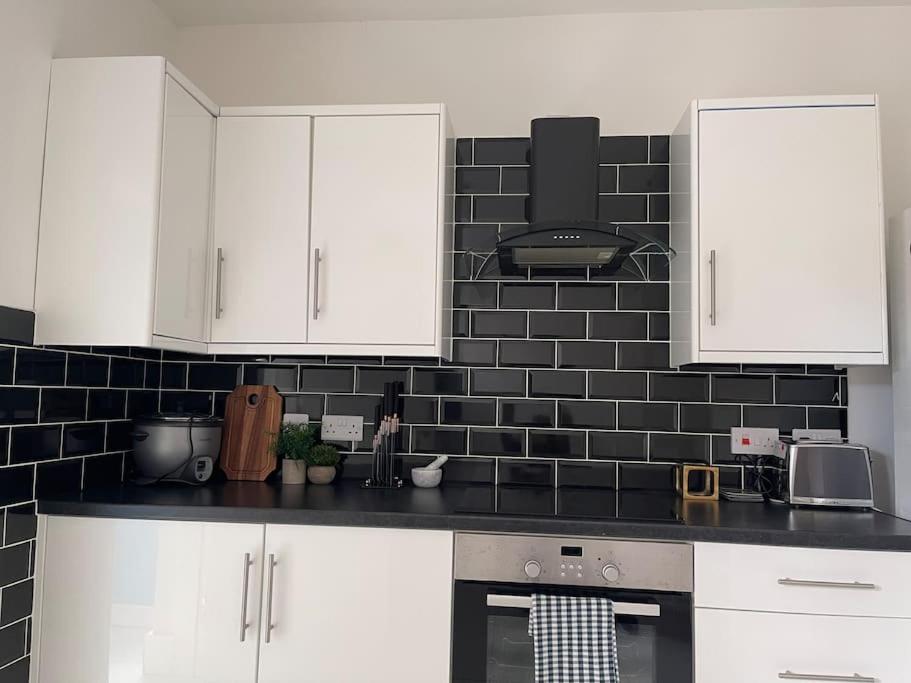 a kitchen with white cabinets and a black tile wall at 2 Bedroom House next to Slade Green Station in Slades Green
