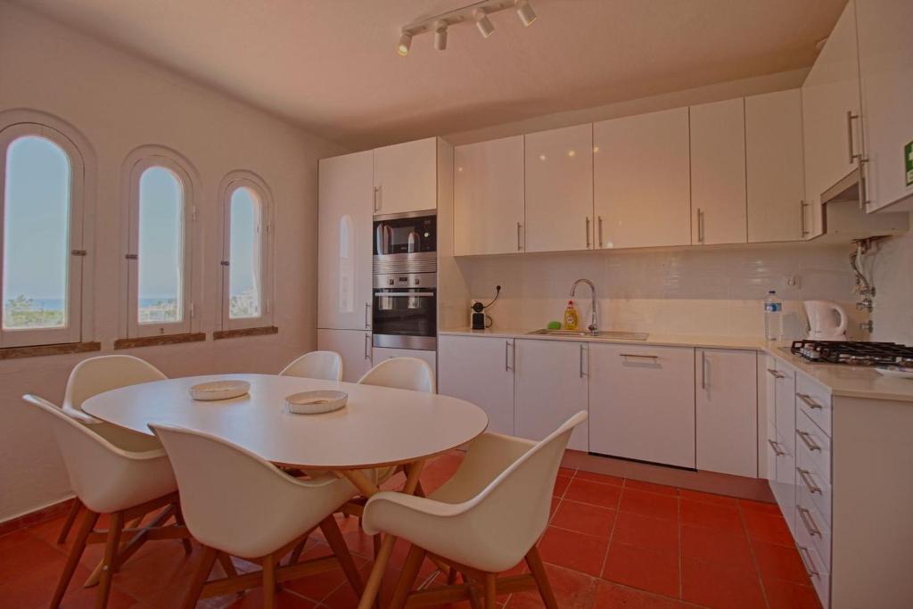 a kitchen with a table and white cabinets and chairs at Apartamento Olhos D'Água VistaBella in Olhos de Água