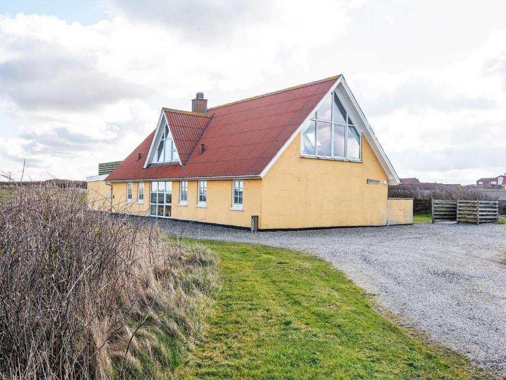 a yellow house with a red roof on a gravel road at 12 person holiday home in Lemvig in Ferring