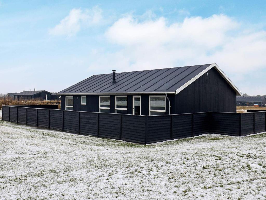 uma casa preta com um telhado preto num campo em 6 person holiday home in L kken em Lokken