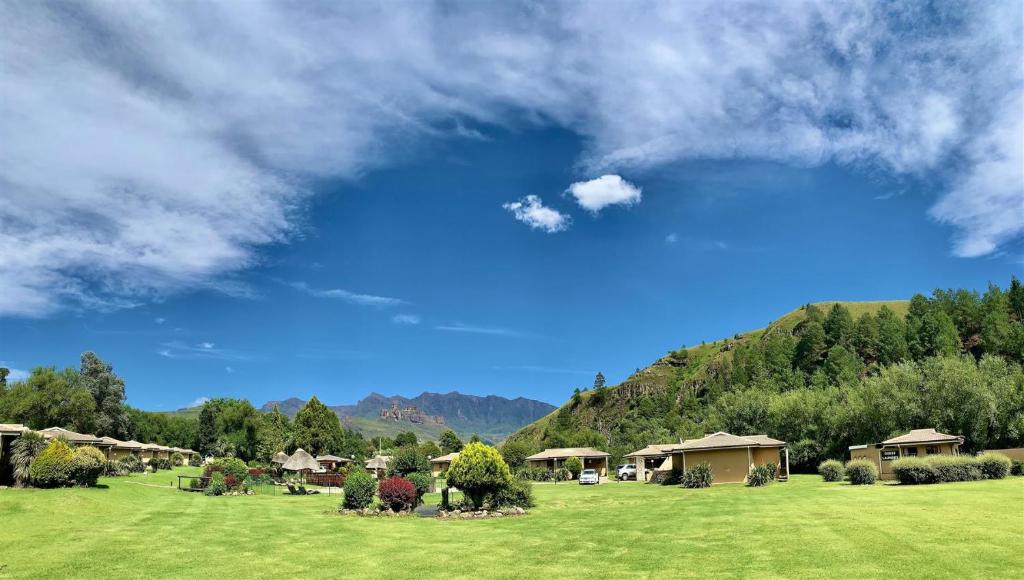 un campo verde con casas y un cielo azul en Gooderson Leisure Riverbend Chalets Self Catering and Timeshare Gold Crown Resort, en Drakensberg Garden