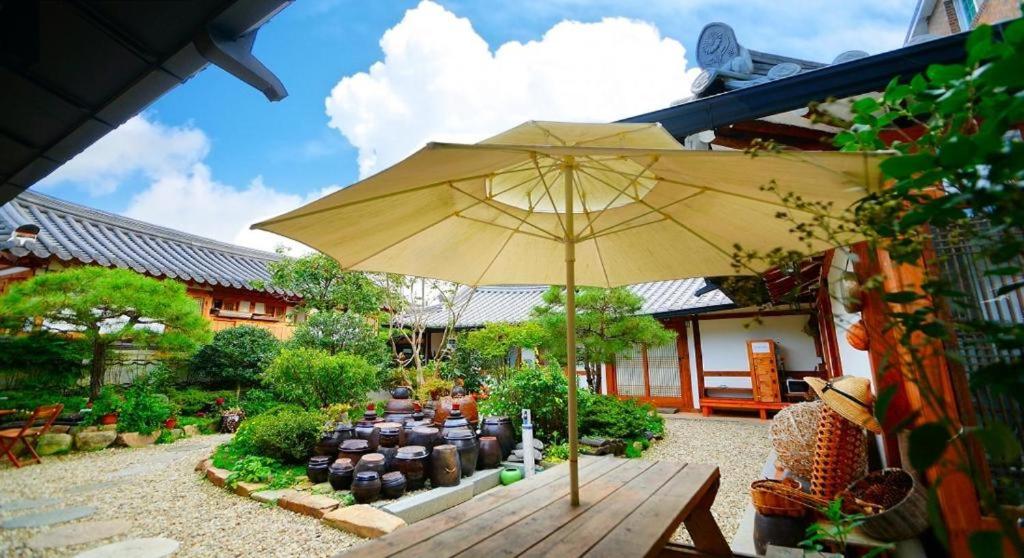 un grande ombrellone giallo in un giardino con panchina di Jeonju Hanok Village Beautiful Garden House a Jeonju
