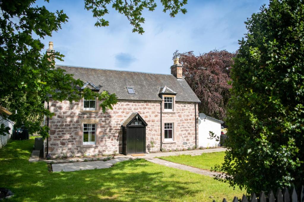 una antigua casa de piedra con un patio verde en Lock Keepers Cottage, Loch Ness Cottage Collection en Inverness