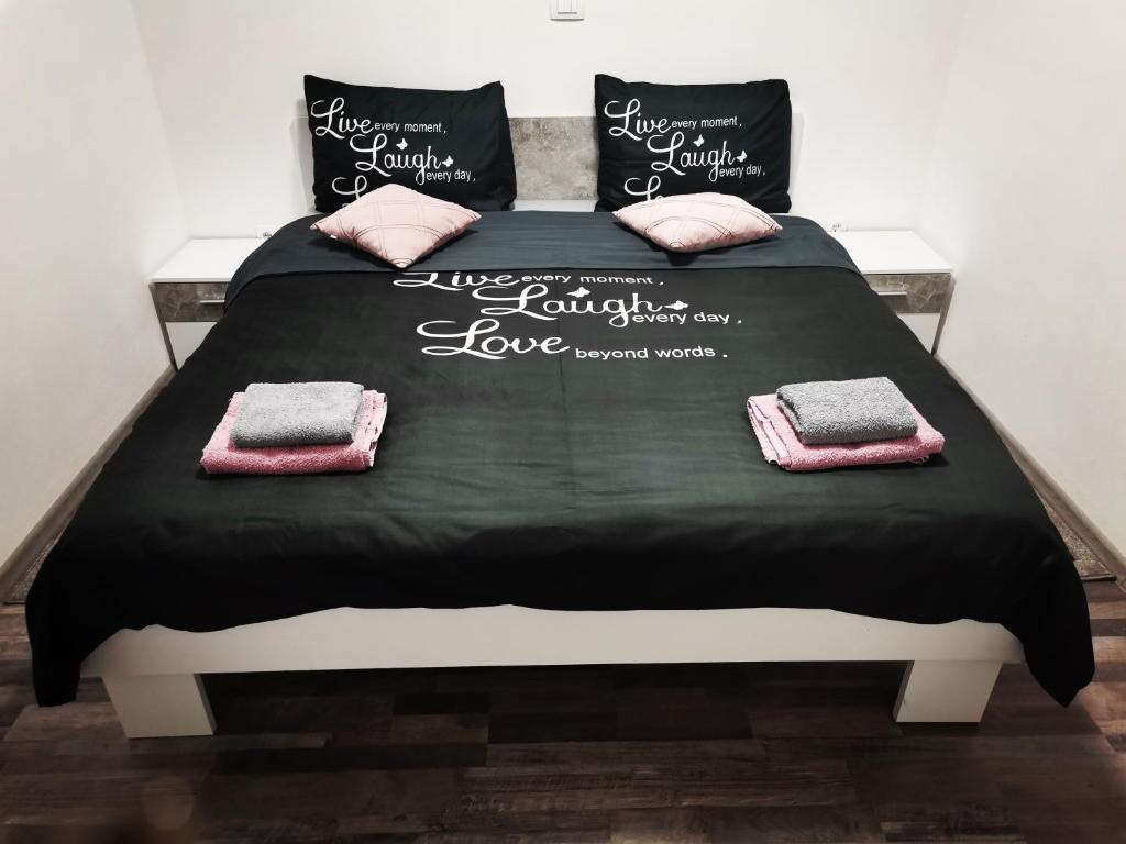 a bed with black sheets and pink pillows on it at Apartmani "Marina" in Otočac