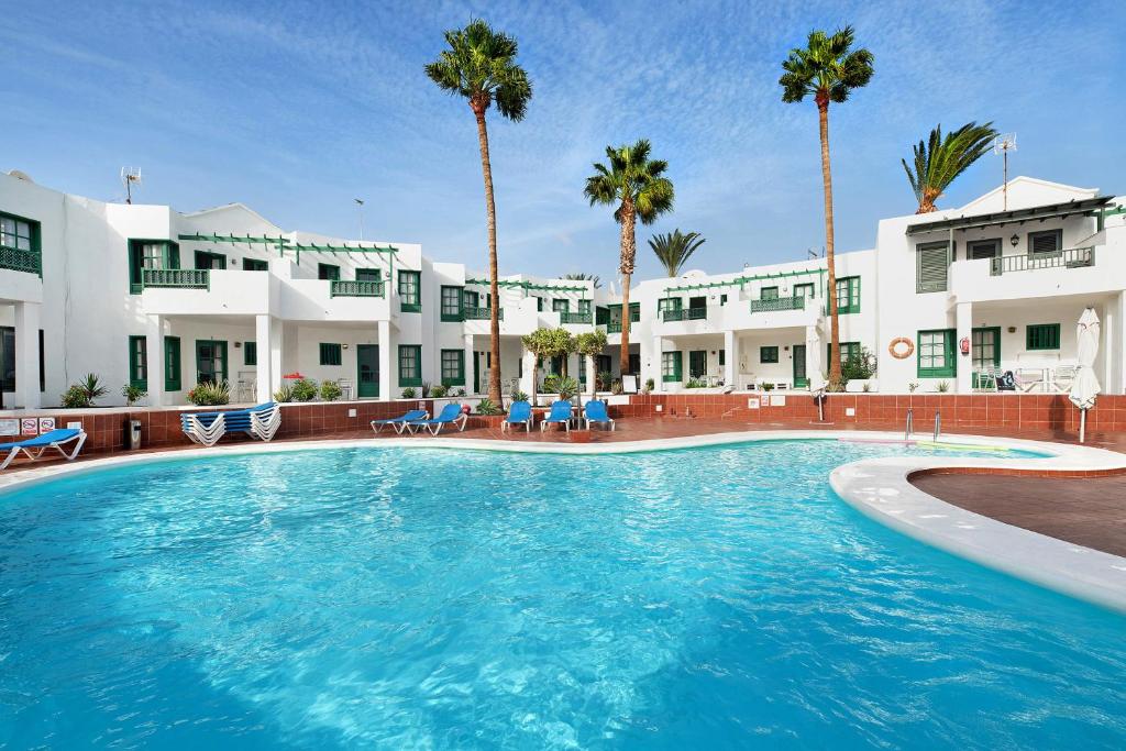 een groot zwembad tegenover een hotel met palmbomen bij Spacious Sunny Relaxing Lanzarote in Puerto del Carmen