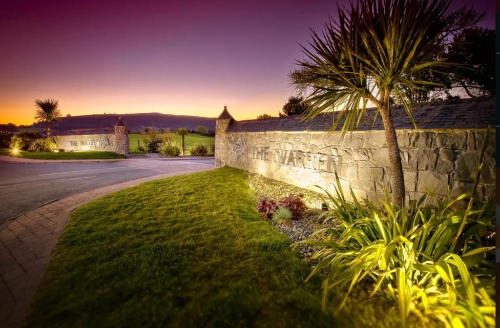 uma palmeira sentada ao lado de uma parede de pedra em The Warren Holiday Park - Family Chalet em Abersoch