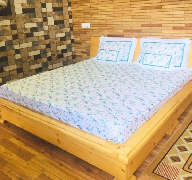 una cama de madera con almohadas azules en una habitación en Anuppam Home Stay, en Kulu