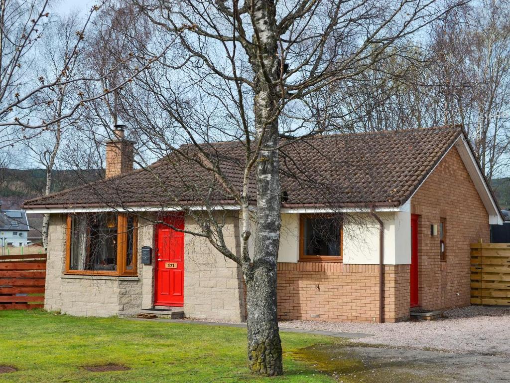 una casa con una porta rossa e un albero di Holly Lodge ad Aviemore