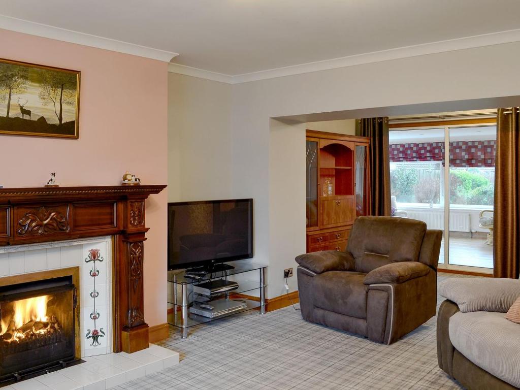 een woonkamer met een open haard, een stoel en een televisie bij Hawthorn Cottage in Stranraer