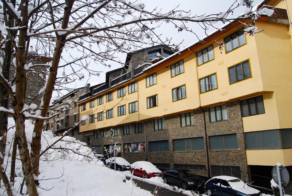 un grande edificio giallo con auto parcheggiate nella neve di Apartaments Del Meligar a Encamp