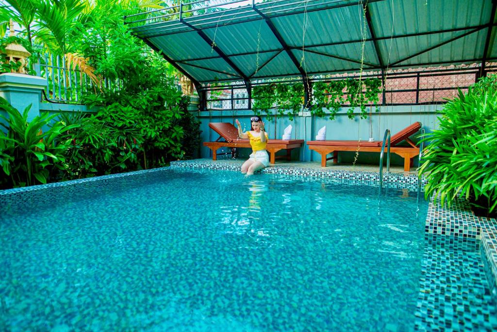 a woman sitting on a chair next to a swimming pool at Mohasal Angkor Boutique in Siem Reap