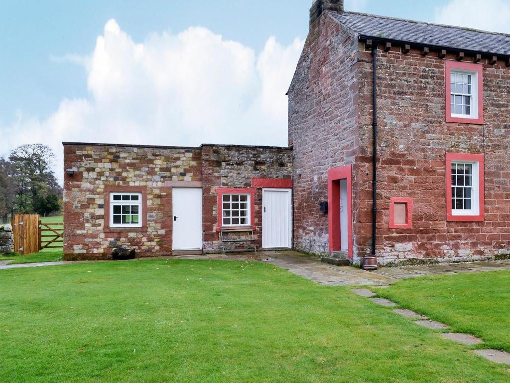 an old brick building with red doors and a yard at The Cottage At 1710 in Castle Carrock