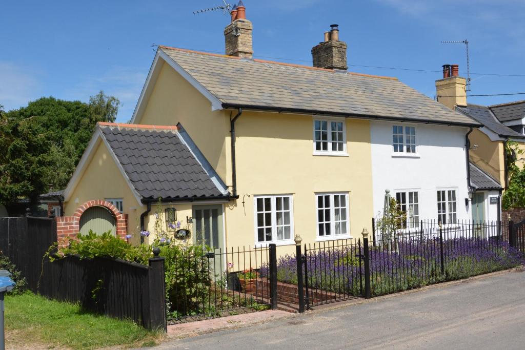 uma casa amarela com um telhado preto e uma cerca em Flaxen Cottage, Heveningham em Heveningham
