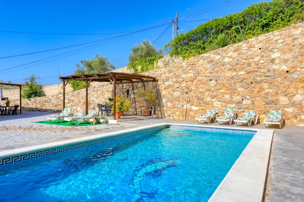 a swimming pool with chairs and a stone wall at Cortijo Montes I in Cómpeta