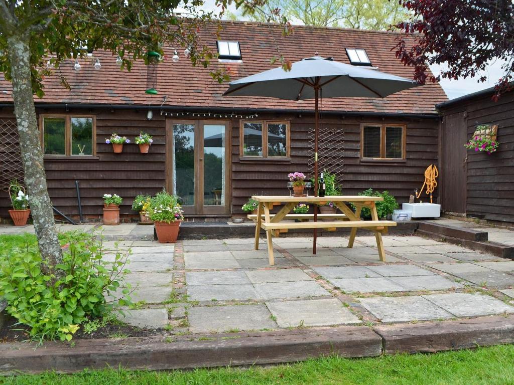 a patio with a wooden table and an umbrella at Honey Meadow Cottage in West Hoathley