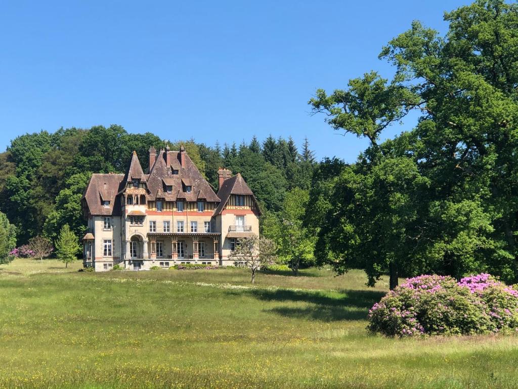 una casa vieja en un campo con árboles y flores en Chateau du Gue aux Biches en Bagnoles de l'Orne