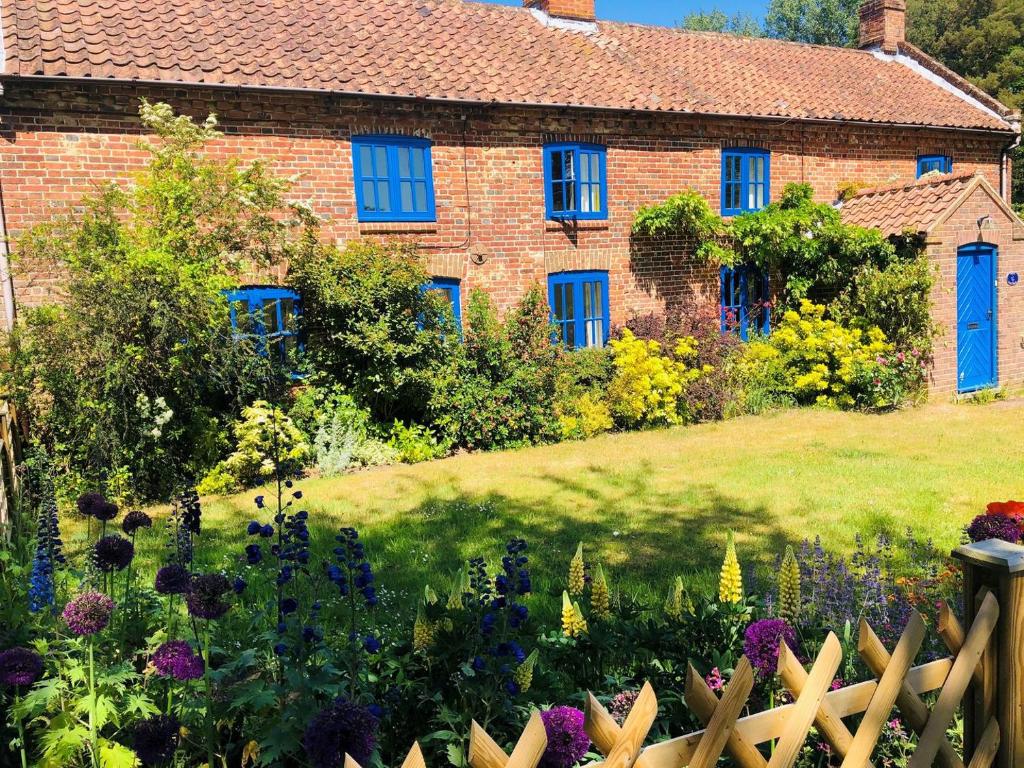 una casa con finestre blu e un giardino fiorito di Dyes Cottage a Hindolveston