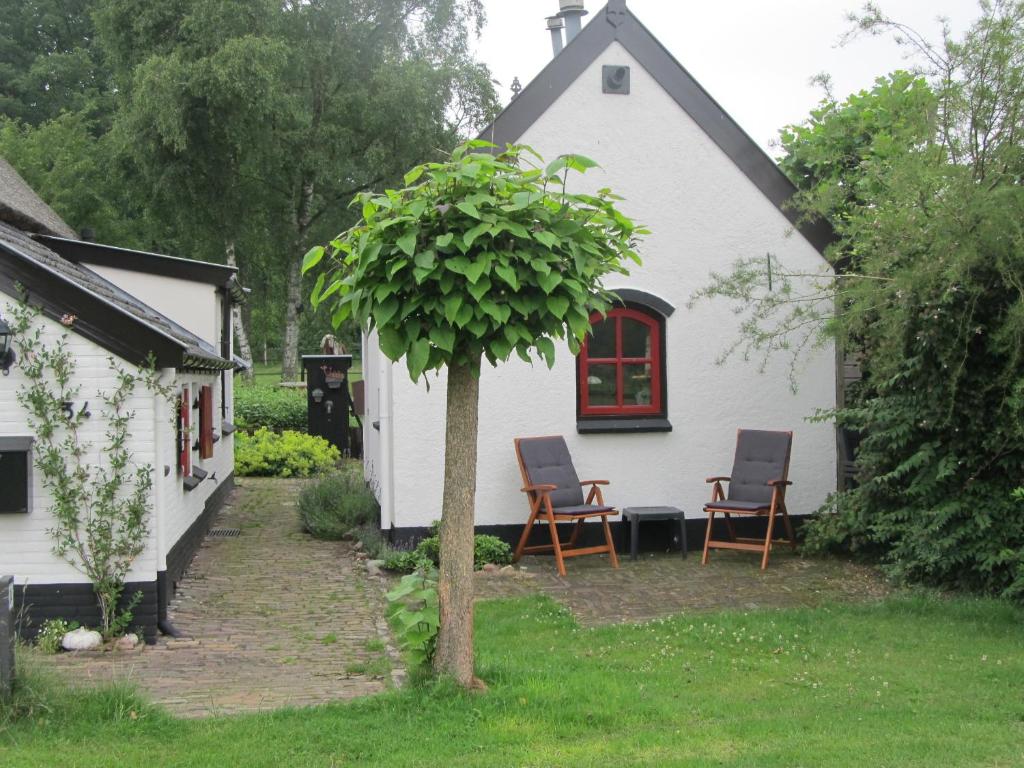 a white house with two chairs and a tree at B&B Het Bakhuis in Loenen