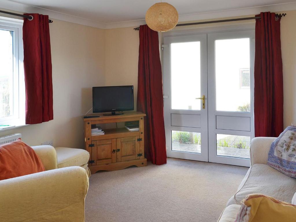 a living room with a tv and red curtains at Lambs Gate in Stoke Gabriel