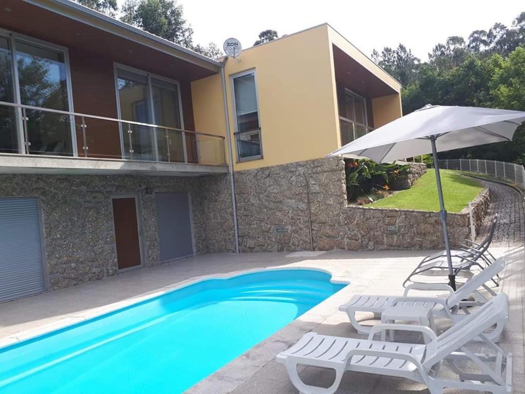 a house with a swimming pool with two chairs and an umbrella at Casa campo ermal in Braga