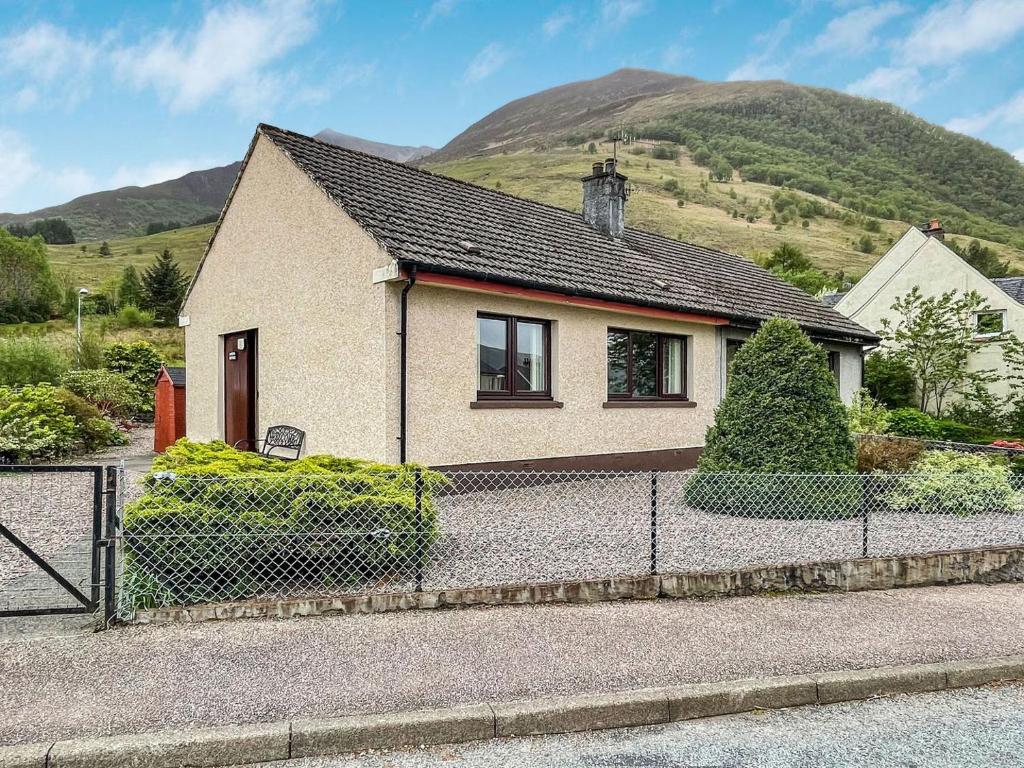 a house with a fence in front of a mountain at Laroch Cottage in Ballachulish