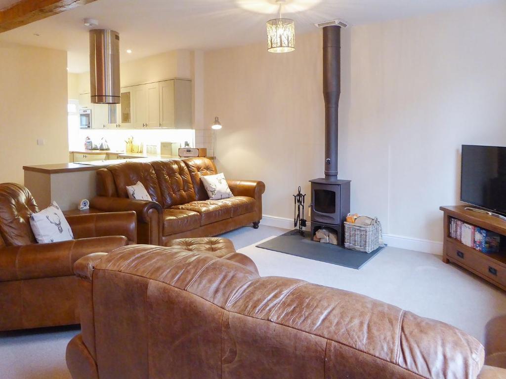 uma sala de estar com mobiliário de couro e um fogão a lenha em Tuppence Cottage em Dulverton