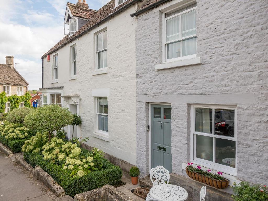 uma casa branca com uma porta azul e alguns arbustos em Cottage On The Green em Calne