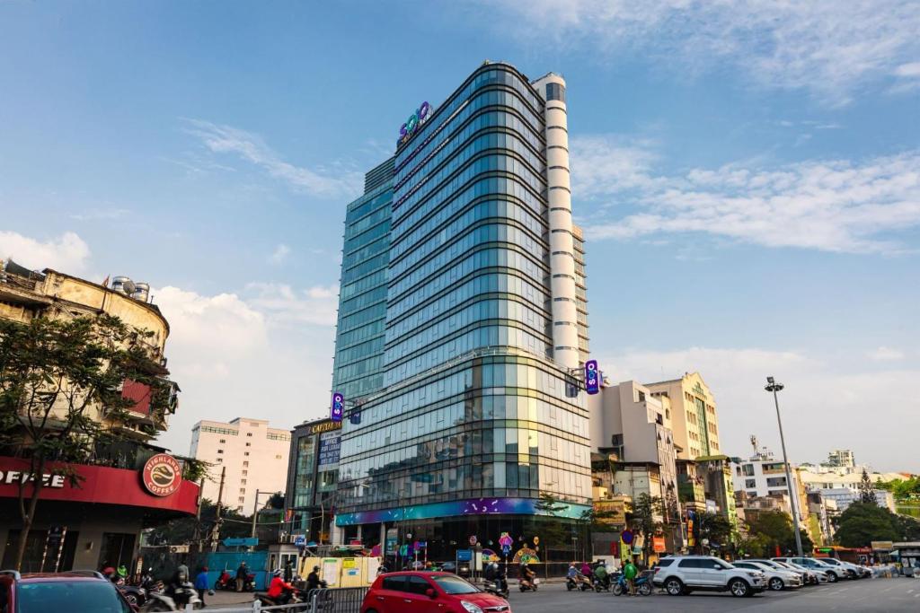 un grand bâtiment en verre dans une rue de la ville avec des voitures dans l'établissement SOJO Hotel Ga Hanoi, à Hanoï