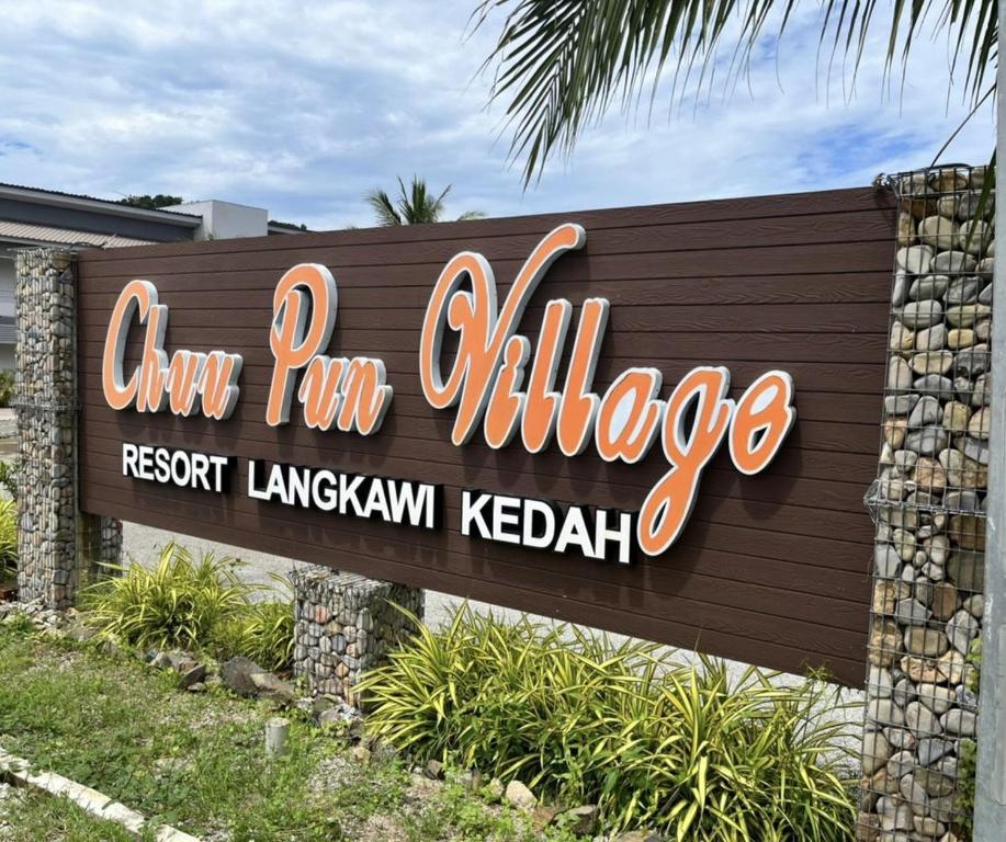 a sign for the entrance to a resort with a palm tree at Chuu Pun Village Resort in Pantai Cenang