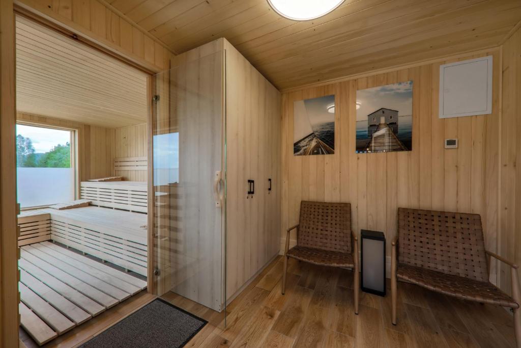 Sauna changing room with two woven chairs, landscape photos, glass door leading to wooden sauna.