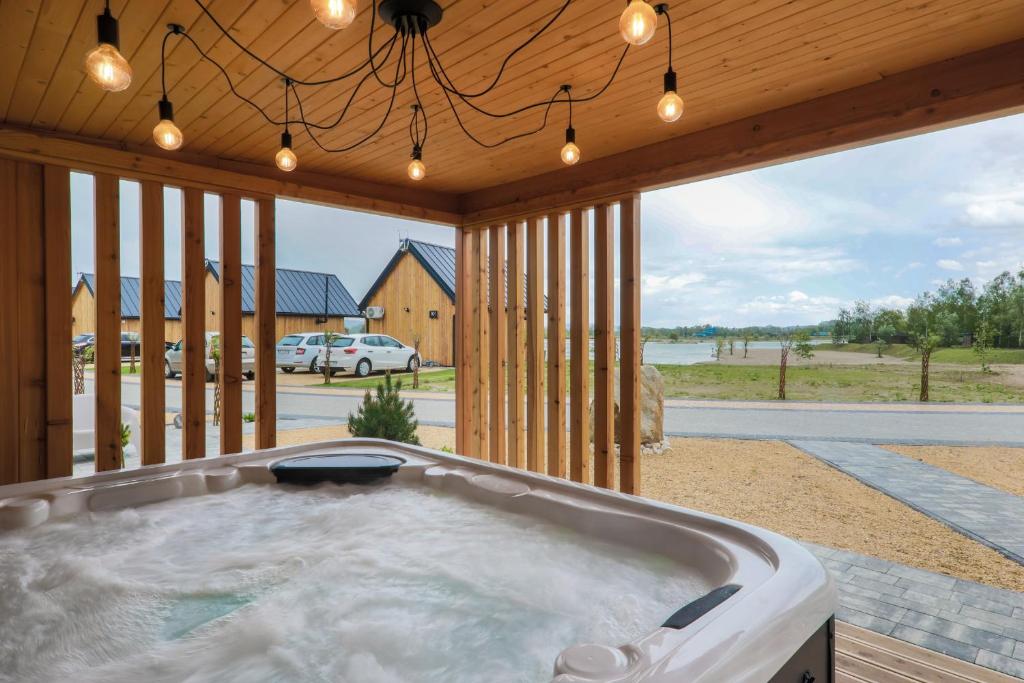 Bubbling hot tub under wooden pergola with hanging bulbs, overlooking road and distant lake.