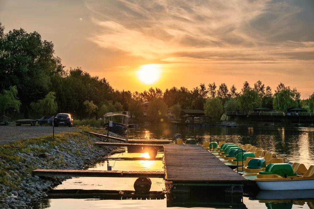 Sunset over lake with wooden dock and lined pedal boats reflecting golden light.