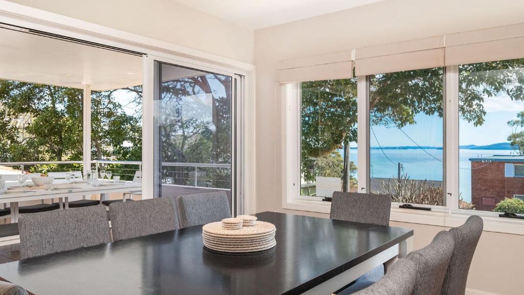 a dining room with a table and chairs and windows at Dutchmans Bay Escape 45A Thurlow in Nelson Bay