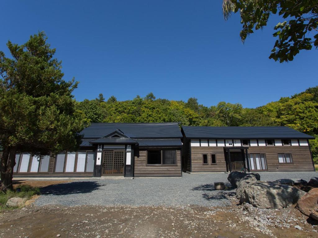 un grand bâtiment en bois avec des arbres en arrière-plan dans l'établissement 古民家の宿 Solii, à Ishikari