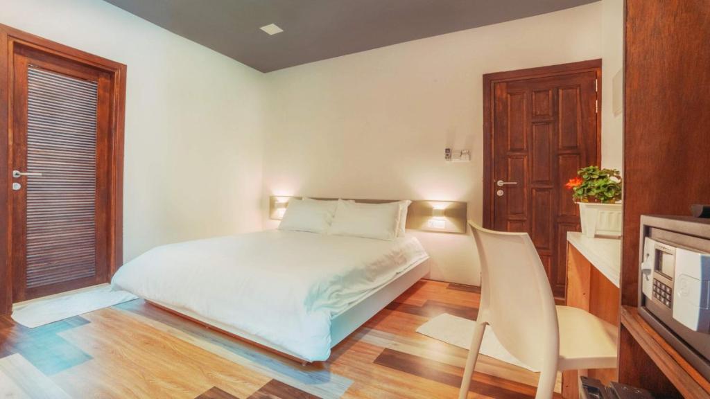 a white bedroom with a bed and a chair at White Coral Rasdhoo in Rasdu