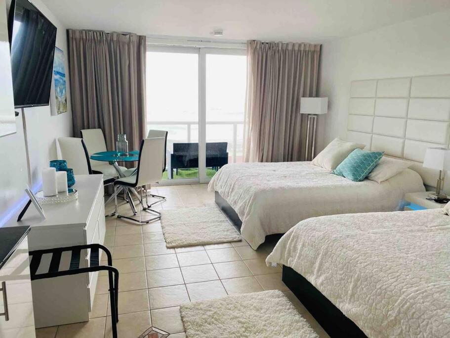 a hotel room with two beds and a desk and a table at Alojamiento con balcon hacia la playa 115 in Miami Beach