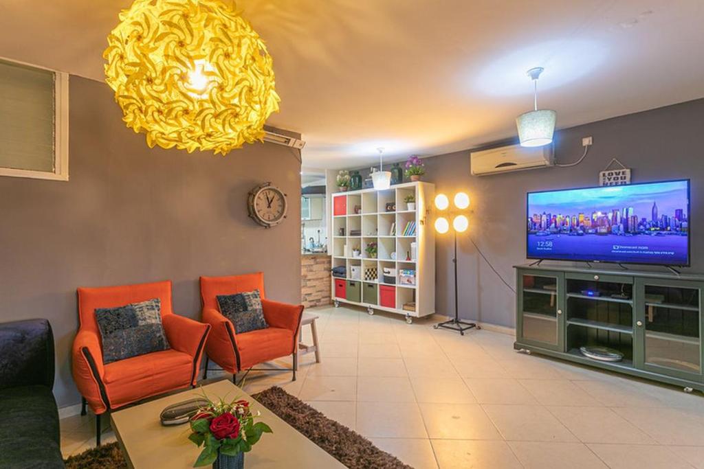 sala de estar con sillas de color naranja y TV de pantalla plana en The Private House רשת הבית הפרטי, en Beer Sheva